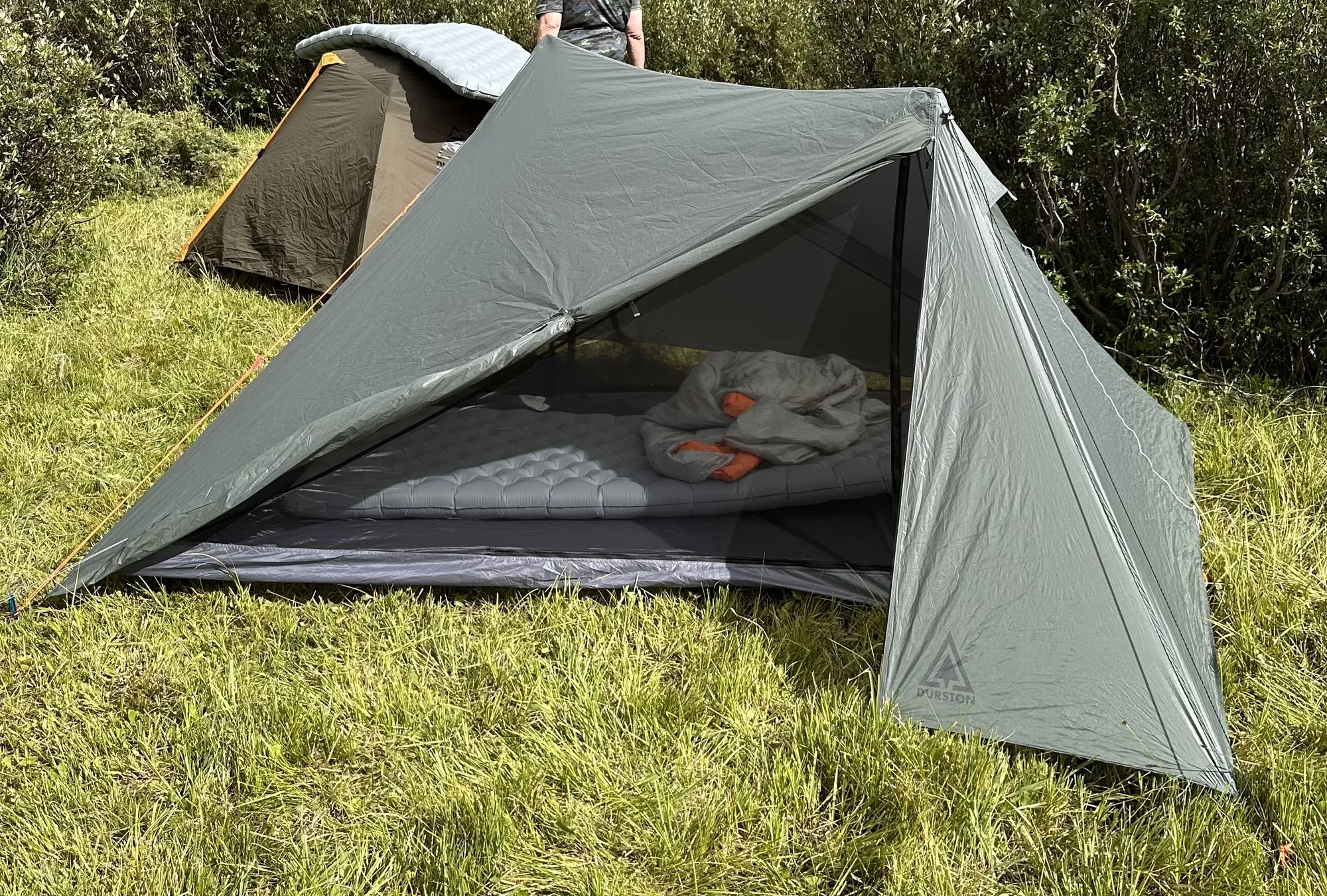 A Durston X-Mid pitched in a grassy meadow with an inflated pad and quilt inside, a second tent behind it.